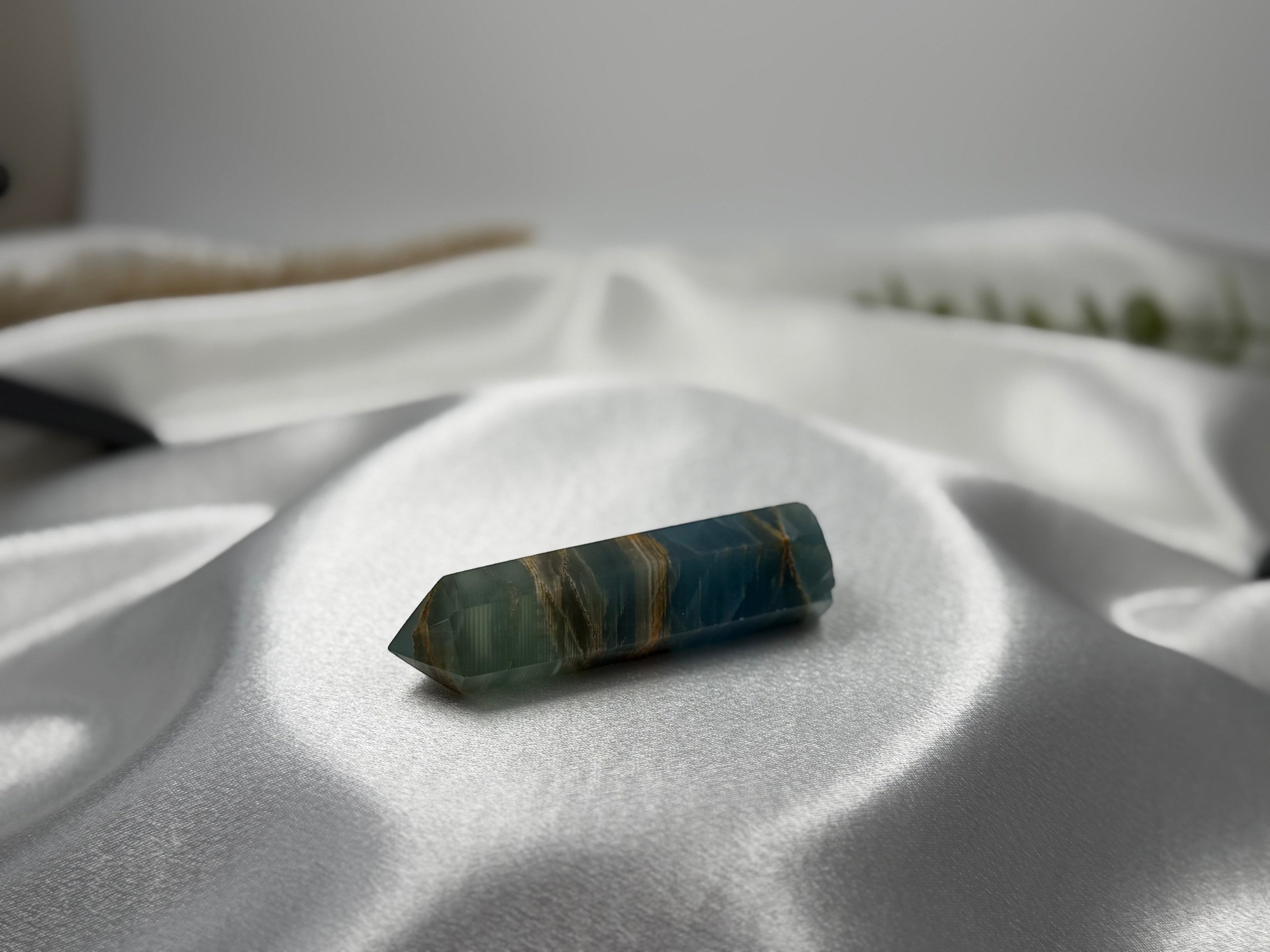 Treasured Energies polished blue onyx crystal tower with natural brown banding resting on white satin fabric.