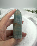 Treasured Energies polished blue onyx crystal tower held in hand against a soft white fabric background.