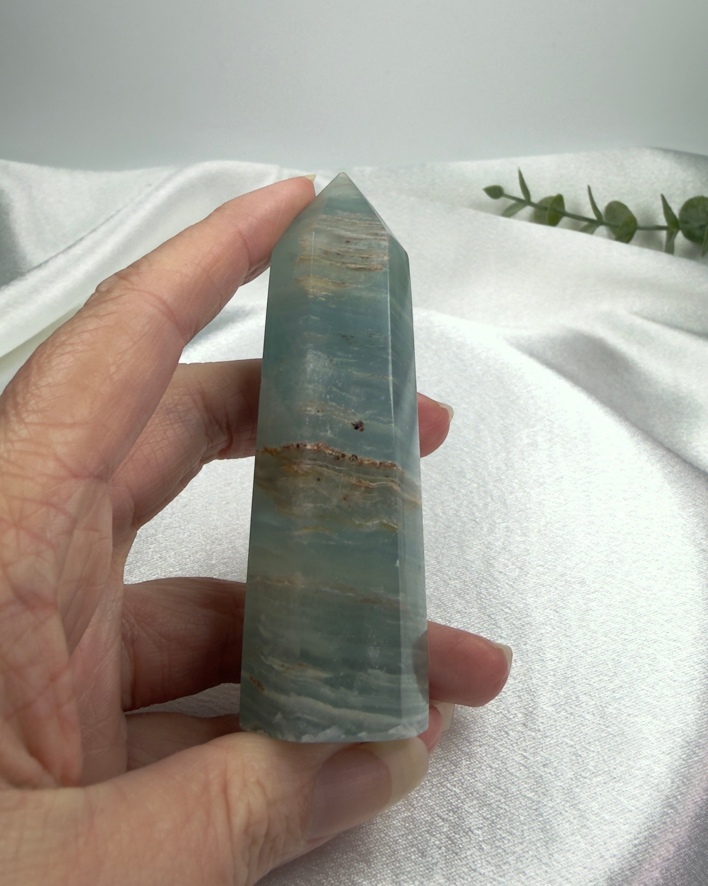Treasured Energies polished blue onyx crystal tower held in hand against a soft white fabric background.