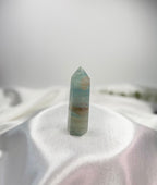 Treasured Energies polished blue onyx crystal tower with natural banding on a white satin fabric background.
