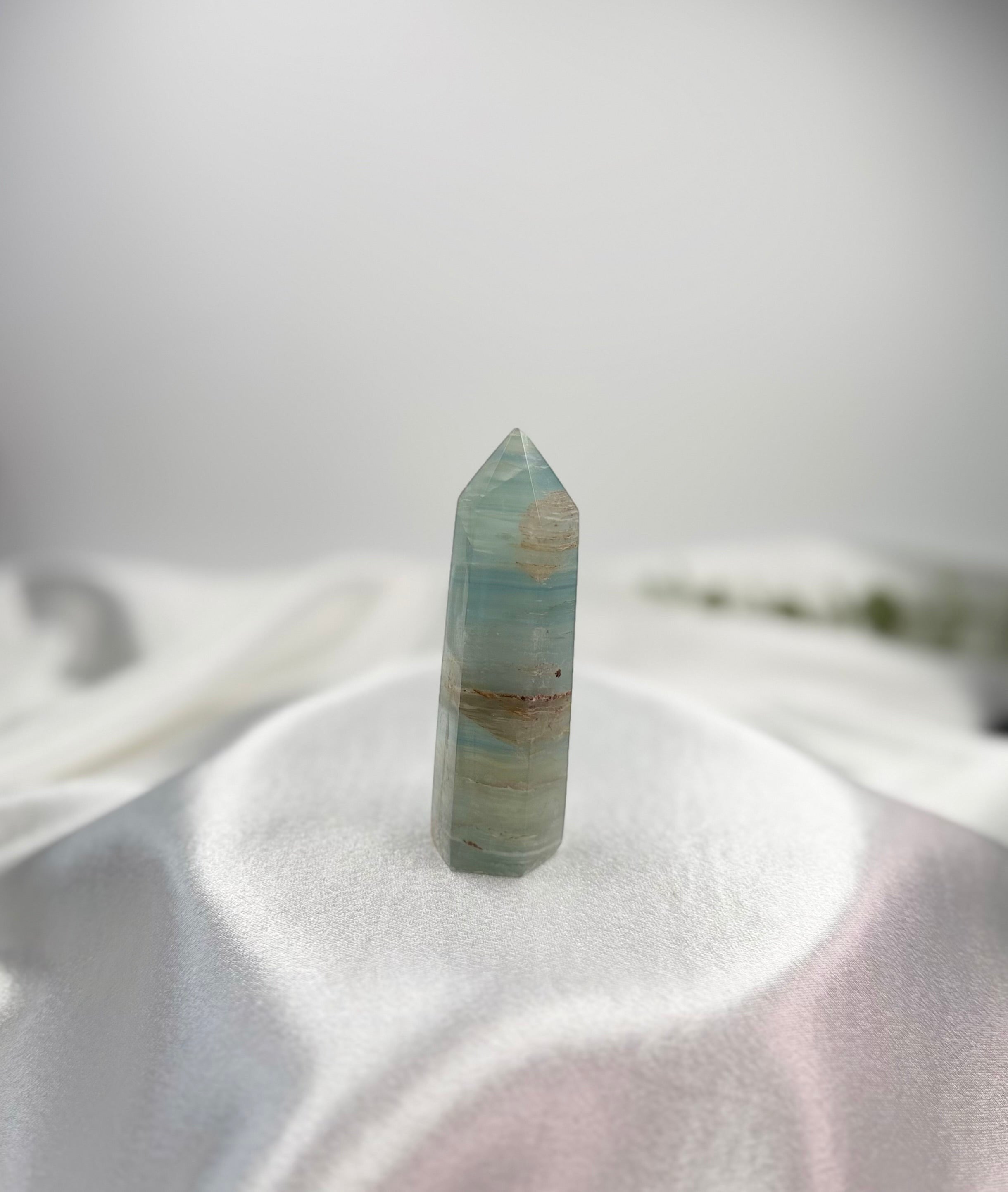 Treasured Energies polished blue onyx crystal tower with natural banding on a white satin fabric background.