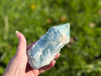 Treasured Energies blue onyx crystal tower with a raw base and polished point held in a hand against a green background
