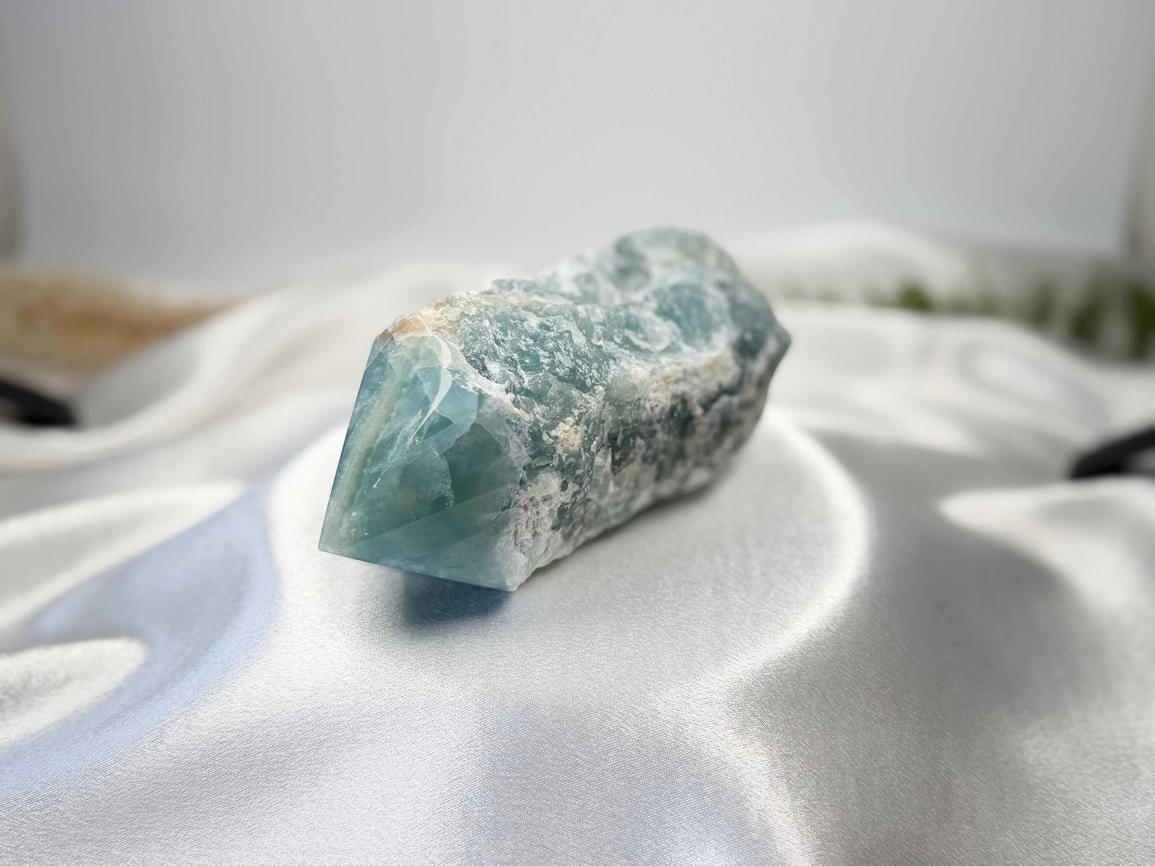 Treasured Energies blue onyx crystal tower with a raw, unpolished base and a smooth, polished point on white silk.