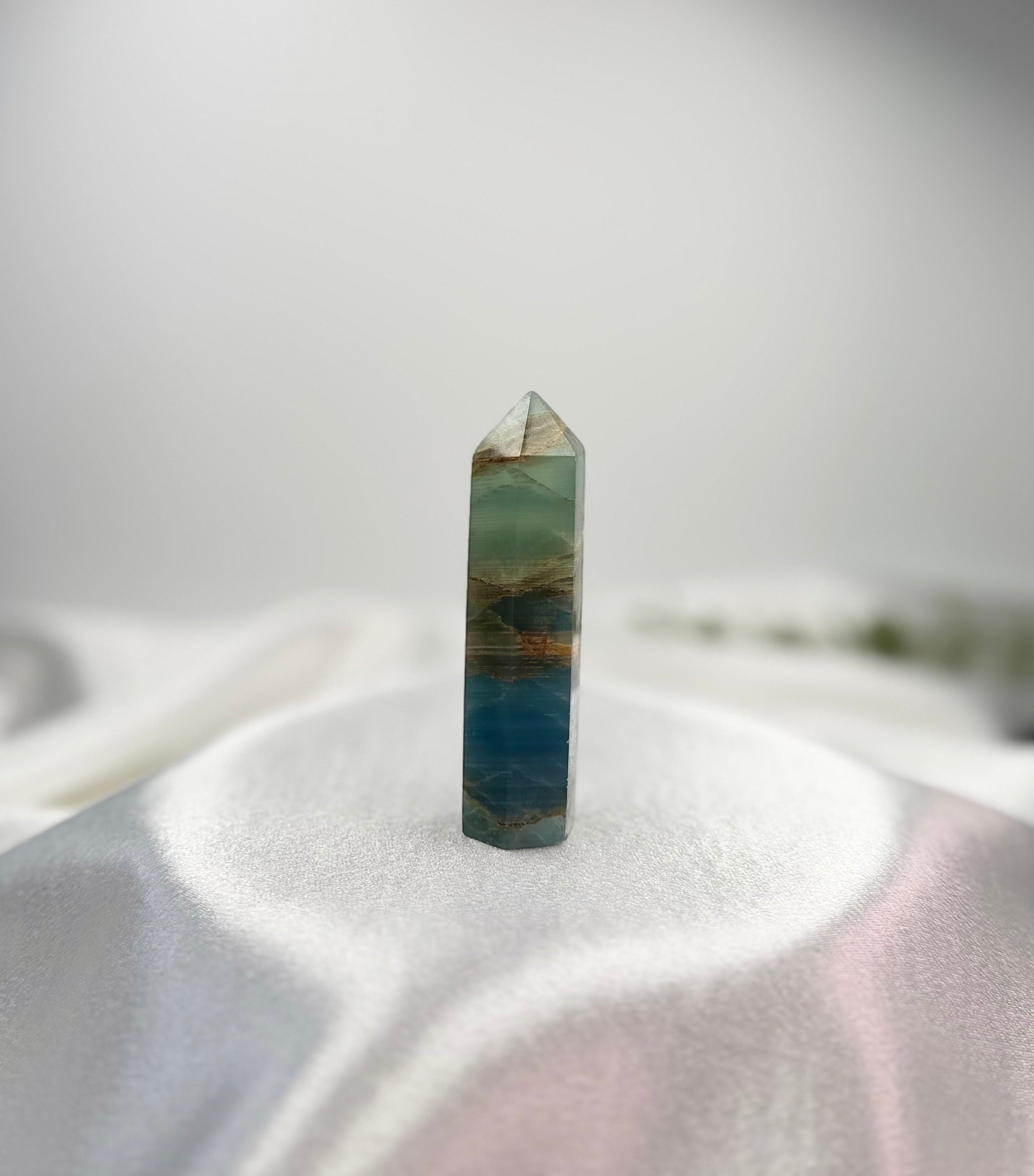 Treasured Energies polished blue onyx crystal tower with natural banding and pointed tip on a white satin surface