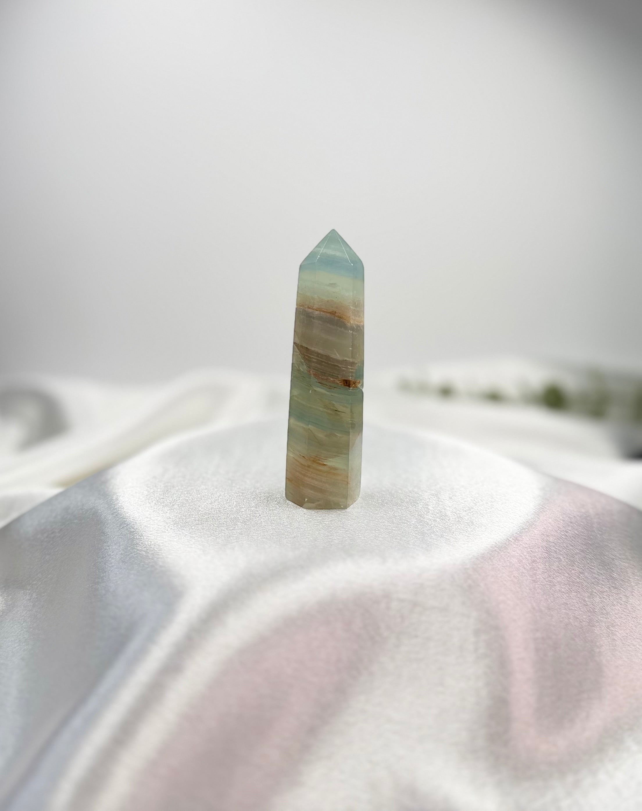 Treasured Energies polished blue onyx crystal tower with natural banding on a white satin fabric background.