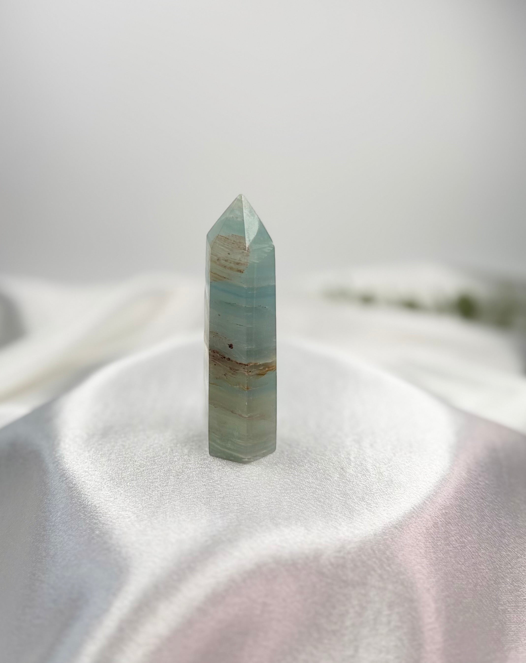 Treasured Energies polished blue onyx crystal tower with natural banding on a white satin fabric background.