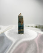 Treasured Energies polished Blue Onyx crystal tower with natural brown banding and a pointed tip on a white surface.