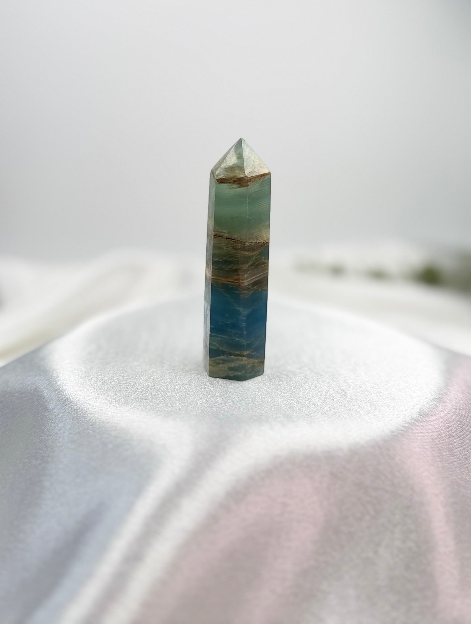 Treasured Energies polished blue onyx crystal tower with natural brown banding on a soft white display surface