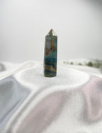 Treasured Energies polished blue onyx crystal tower with natural banding on a soft white fabric background.