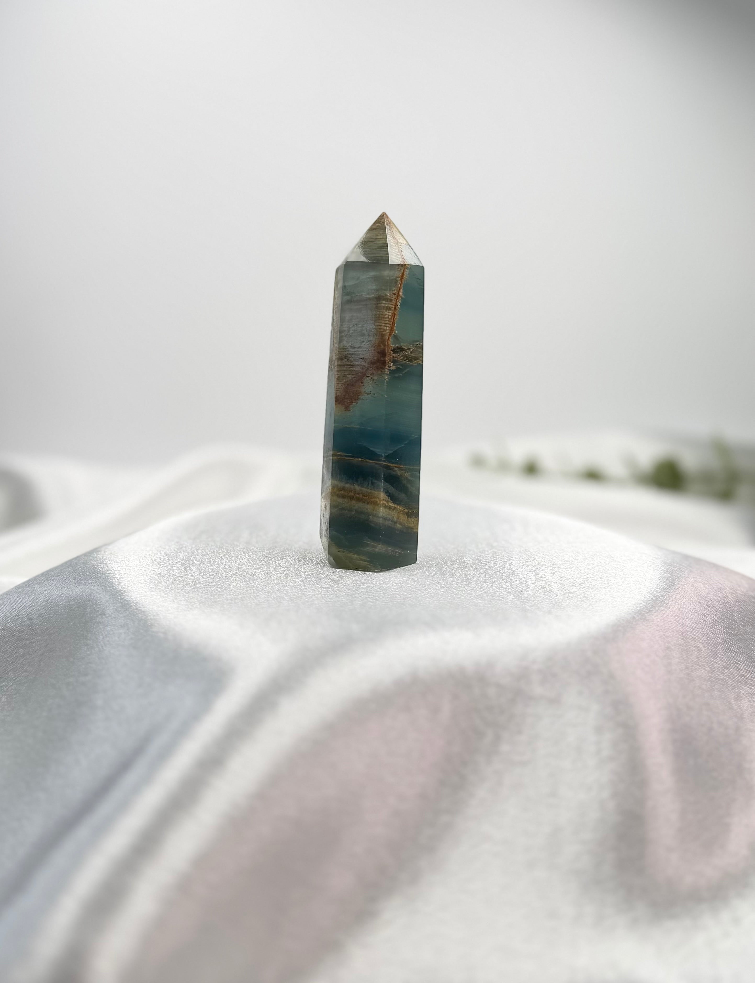 Treasured Energies polished blue onyx crystal tower with natural banding on a soft white fabric background.