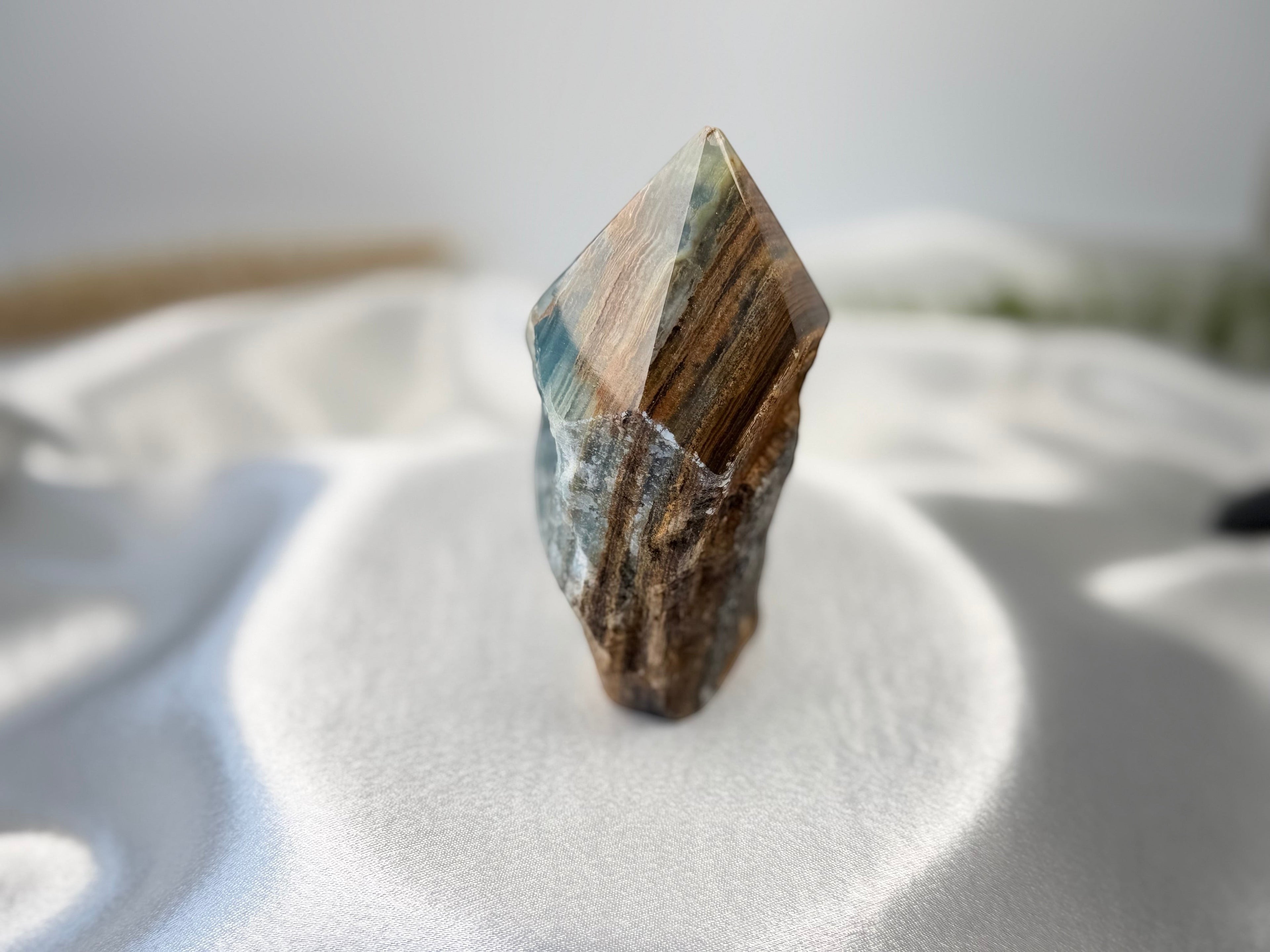 Treasured Energies Blue Onyx crystal tower with a raw, unpolished base and a smooth, faceted point on white silk.