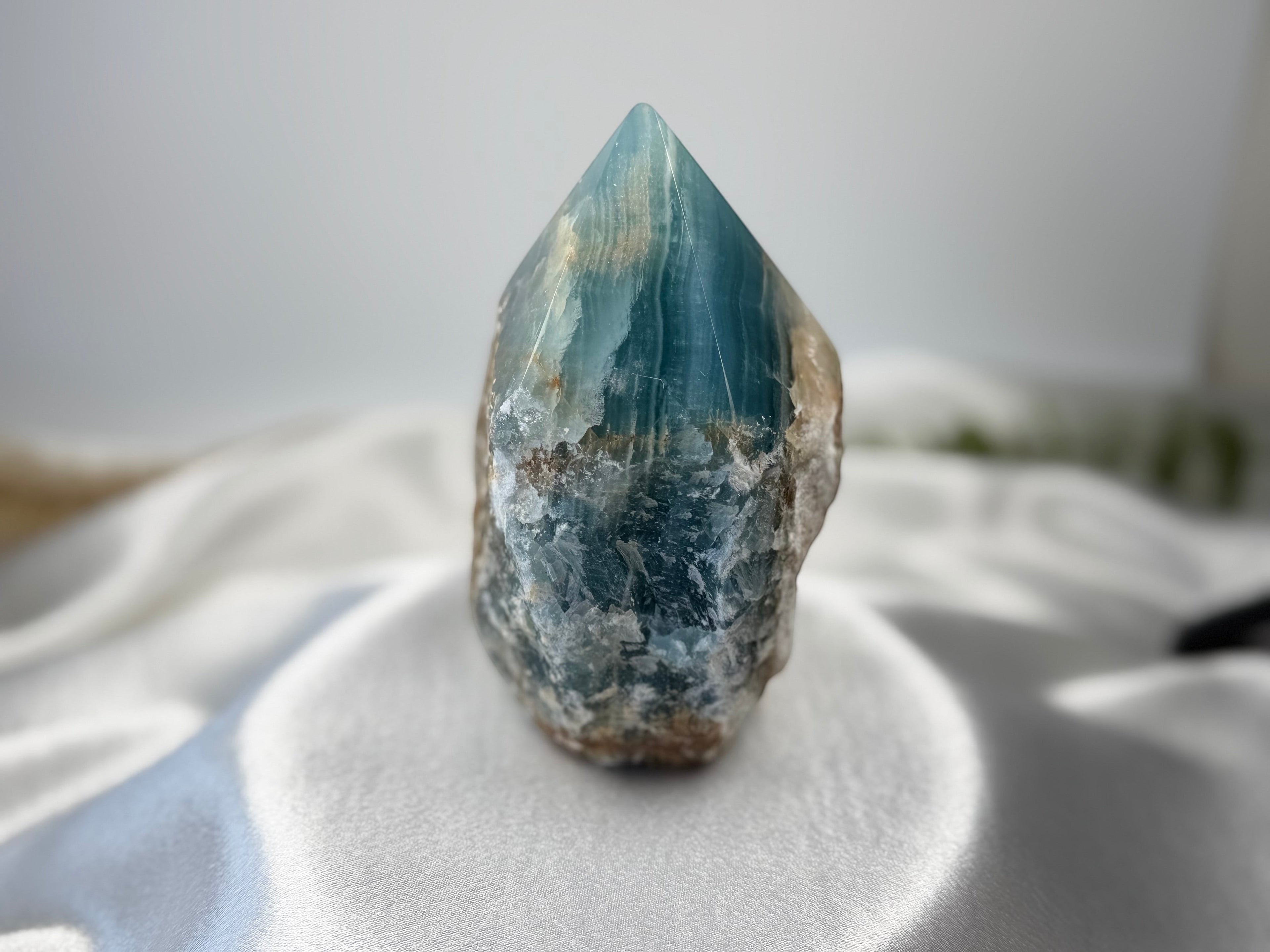 Treasured Energies blue onyx crystal tower with a raw, unpolished base and a smooth, polished point on satin fabric.