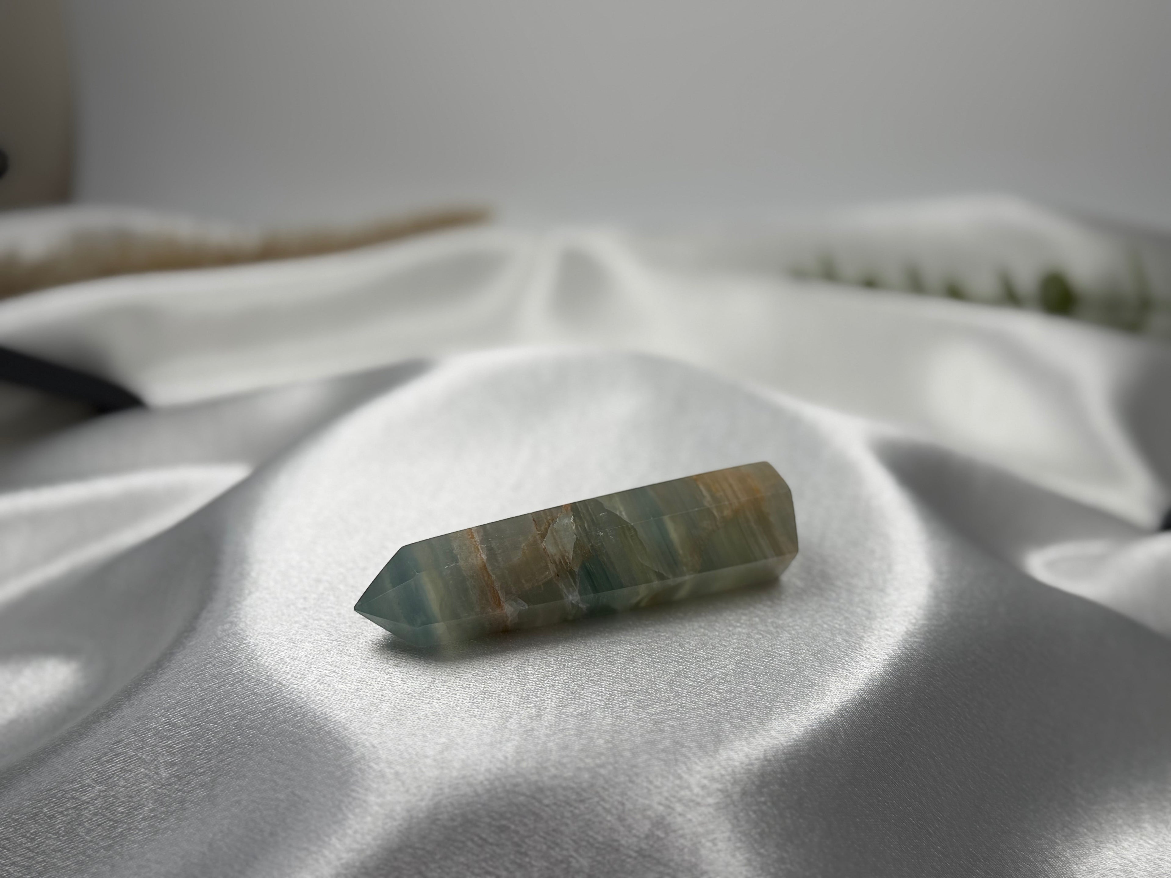 Treasured Energies polished Blue Onyx crystal tower point resting on soft white satin fabric