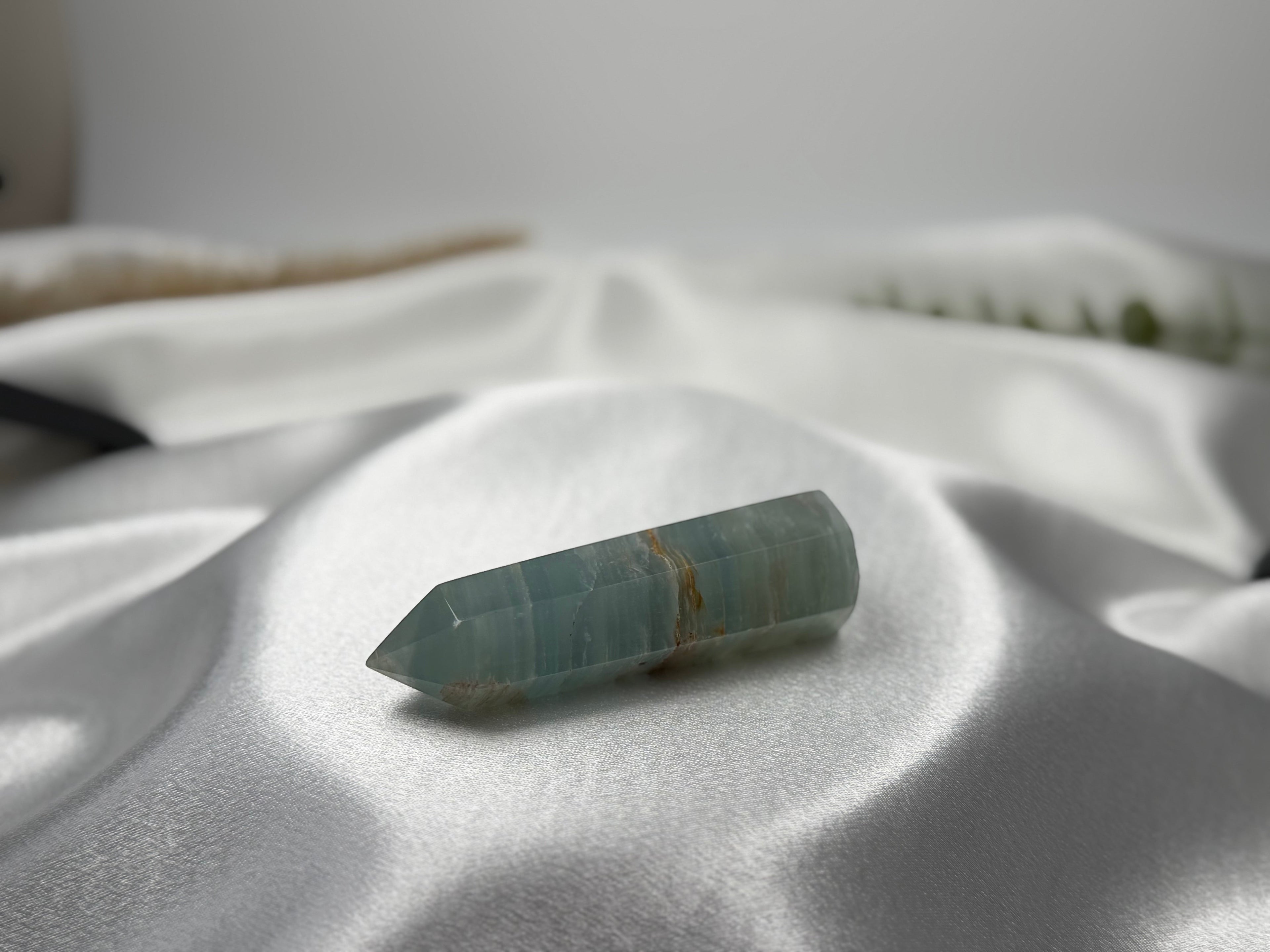 Treasured Energies polished blue onyx crystal tower with natural banding resting on a soft white satin fabric.