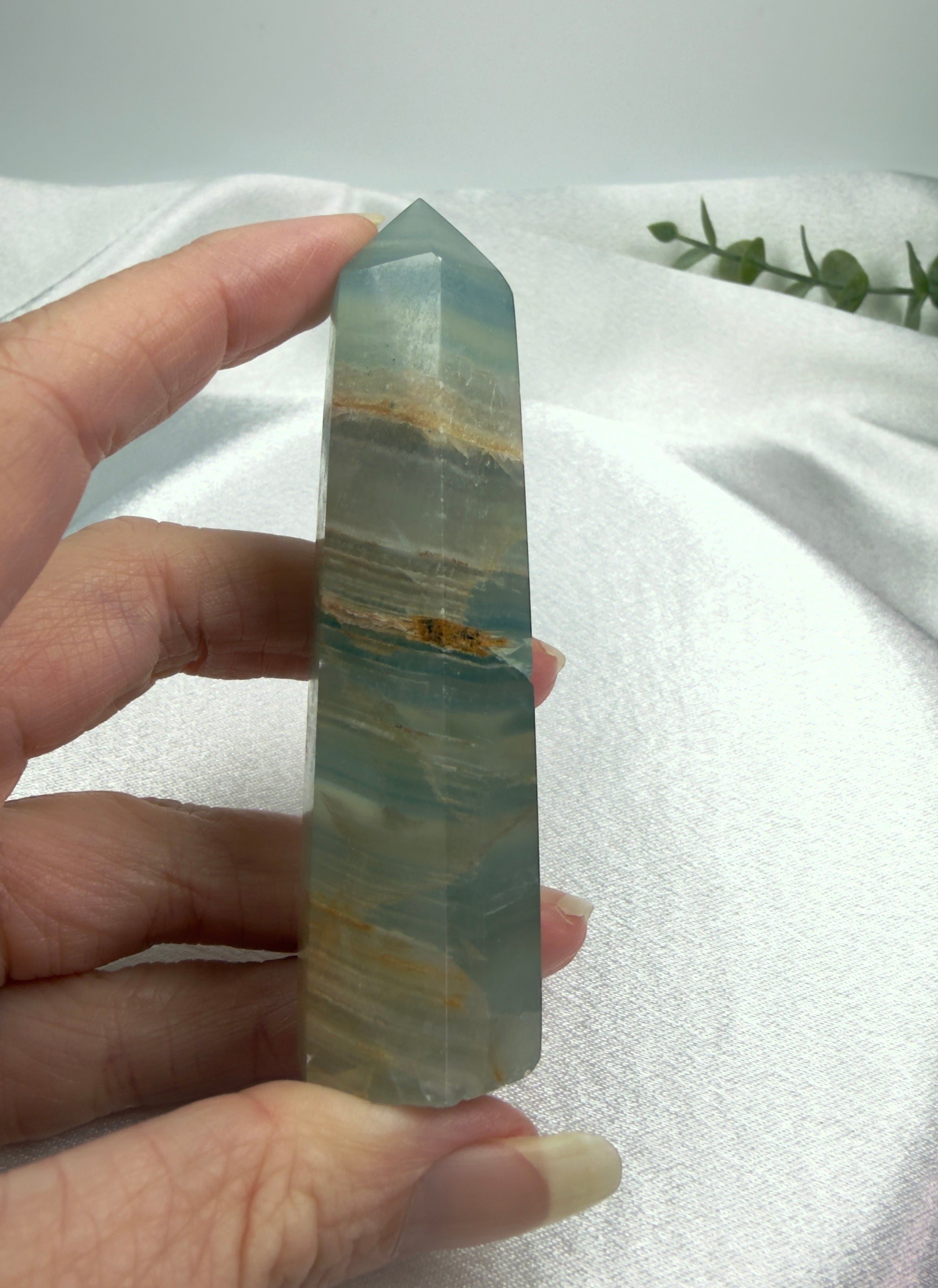 Treasured Energies blue onyx crystal tower held in hand, featuring smooth polished stone with natural banding and point.