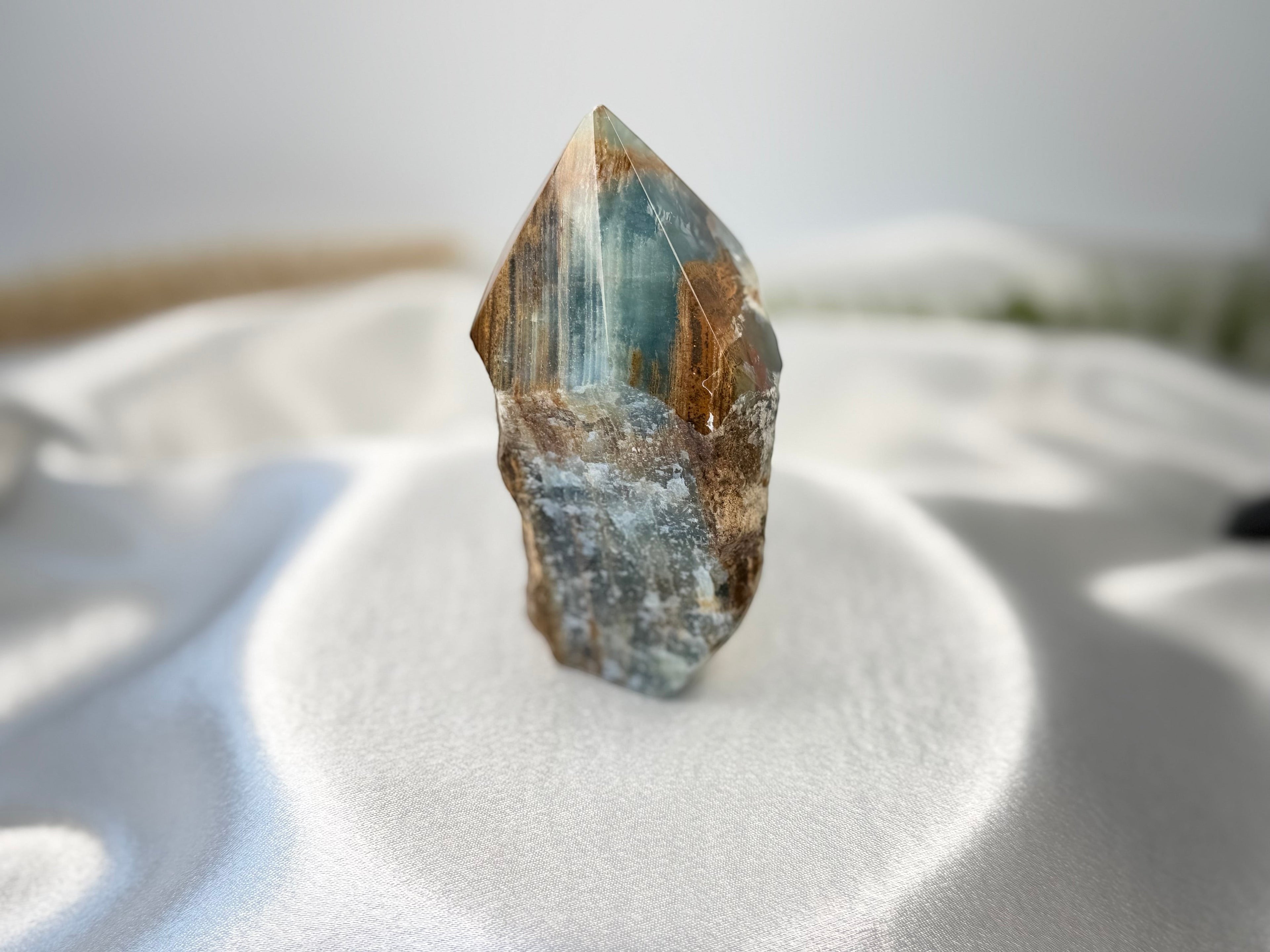 Treasured Energies blue onyx crystal tower with a raw, unpolished base and a smooth, faceted point on white silk.