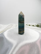 Treasured Energies polished blue onyx crystal tower with natural banding on a white satin cloth background.
