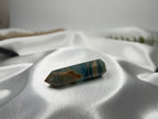 Treasured Energies polished blue onyx crystal tower with natural brown banding resting on white satin fabric.