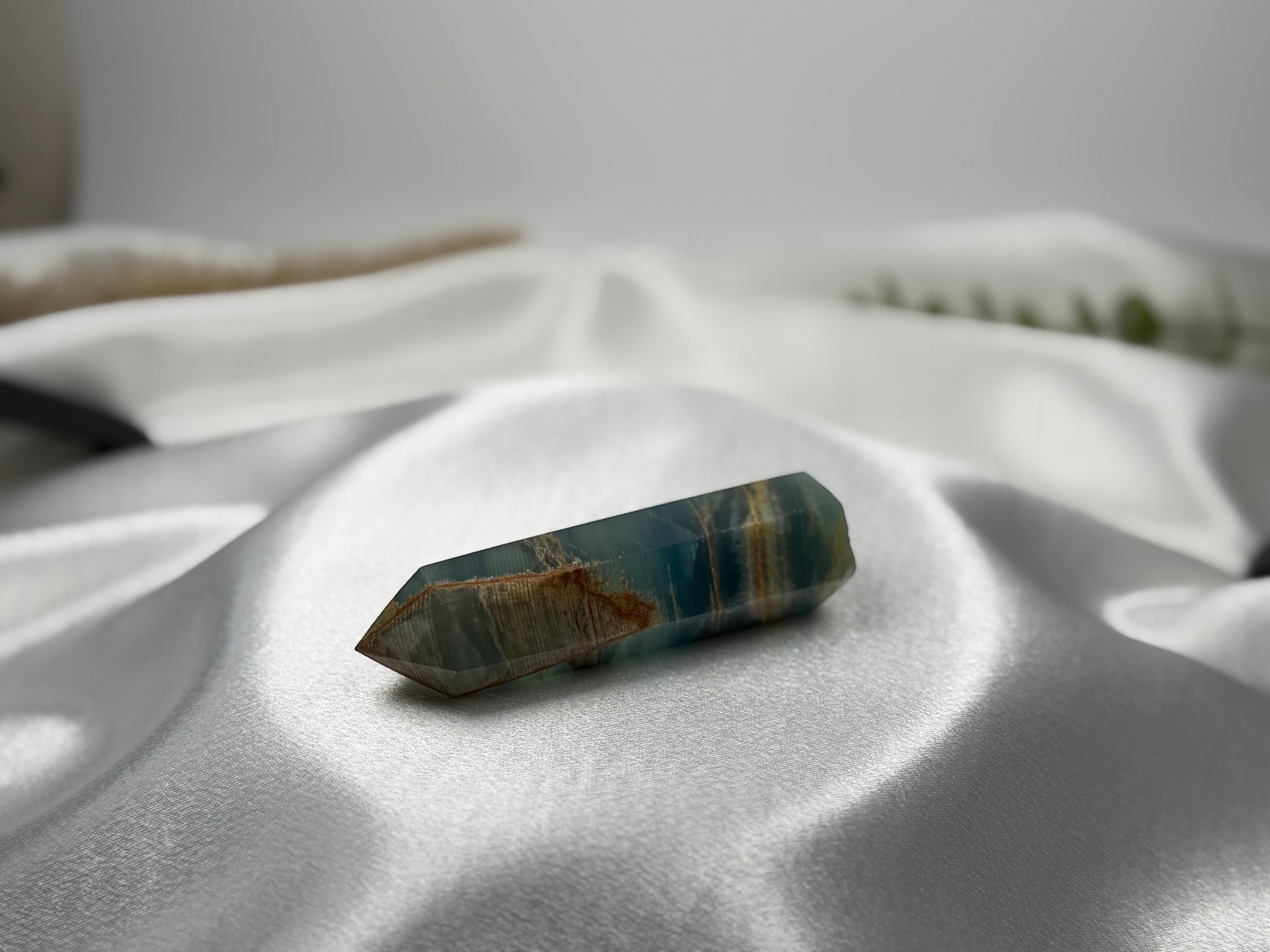 Treasured Energies polished blue onyx crystal tower with natural brown banding resting on white satin fabric.