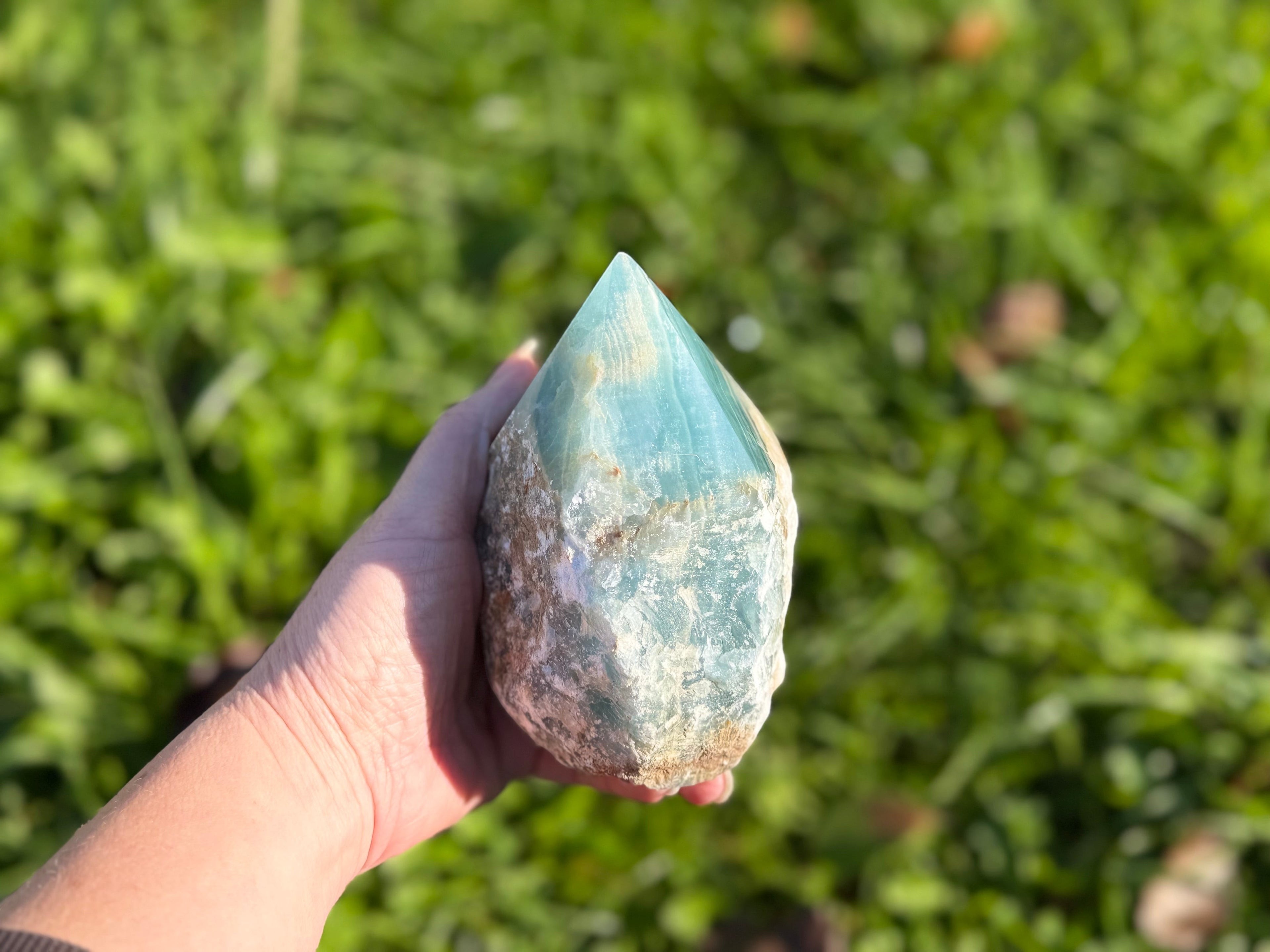 Treasured Energies blue onyx crystal tower with a raw, unpolished base and a smooth, polished point held in a hand.