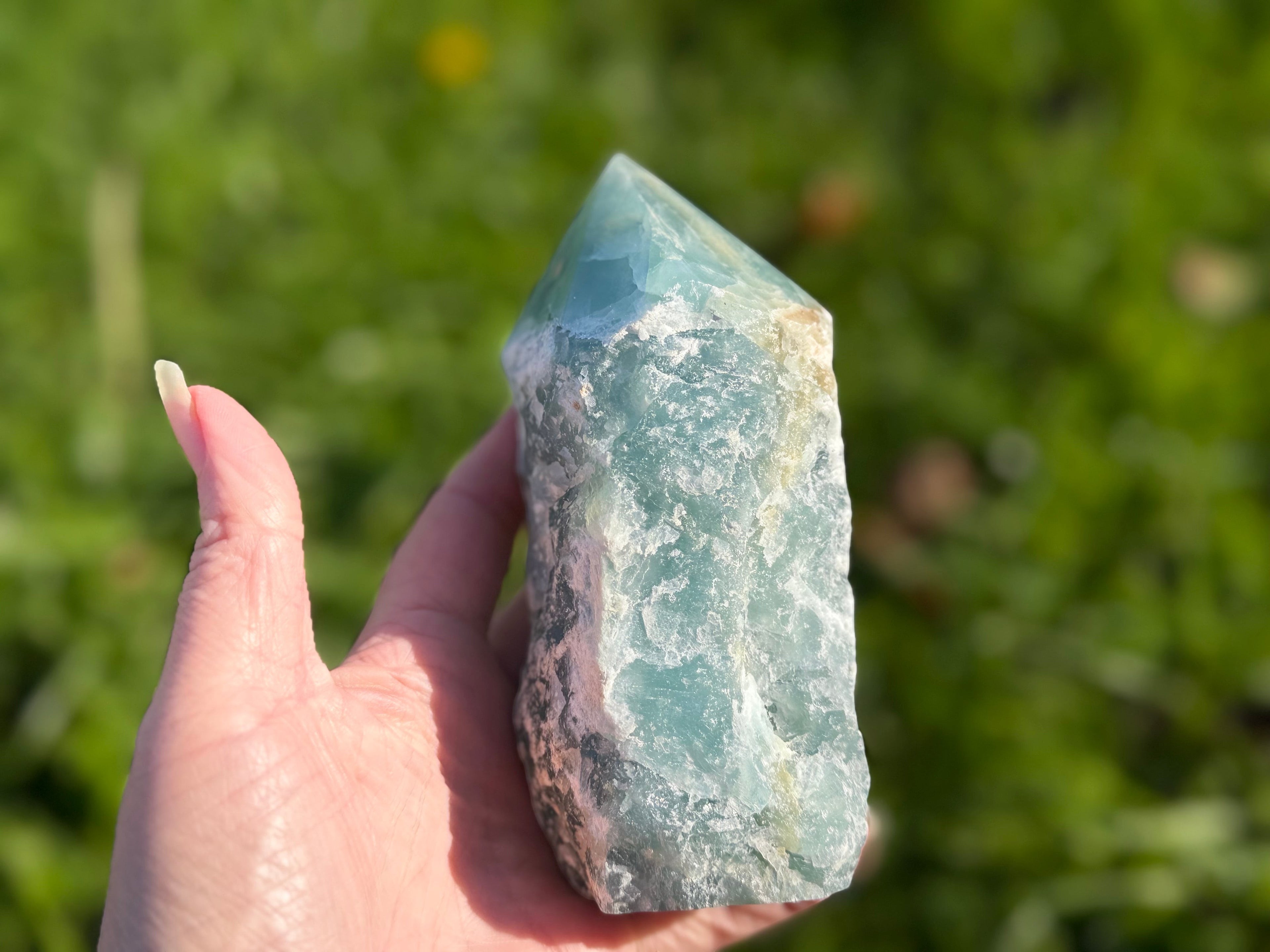 Treasured Energies blue onyx crystal tower with a raw base and polished point held in a hand outdoors