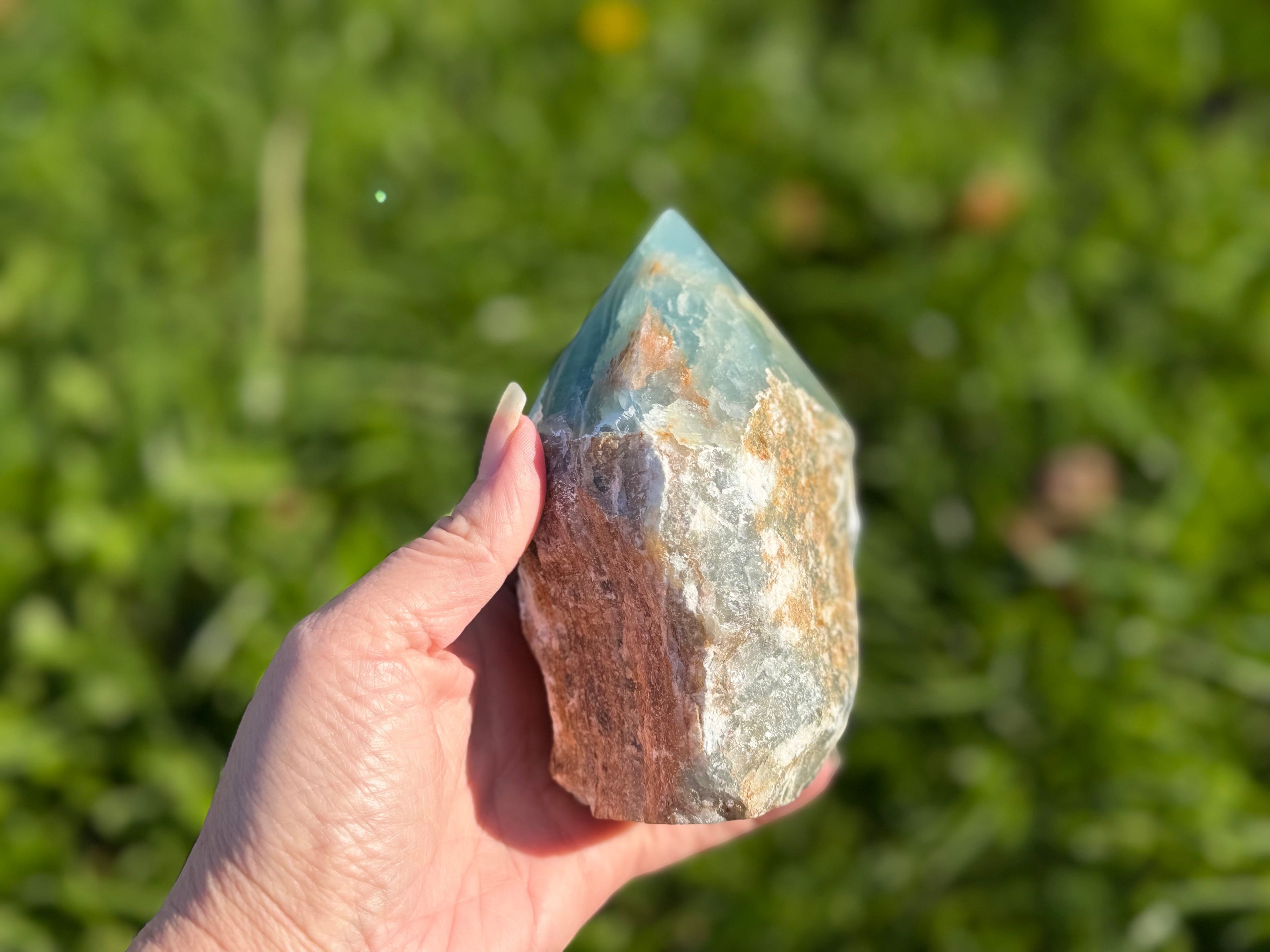 Treasured Energies Blue Onyx crystal tower with a raw, earthy base and a smooth, polished point held in a hand.