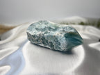 Treasured Energies blue onyx crystal with a raw, natural base and a smooth, polished tower point on white satin.