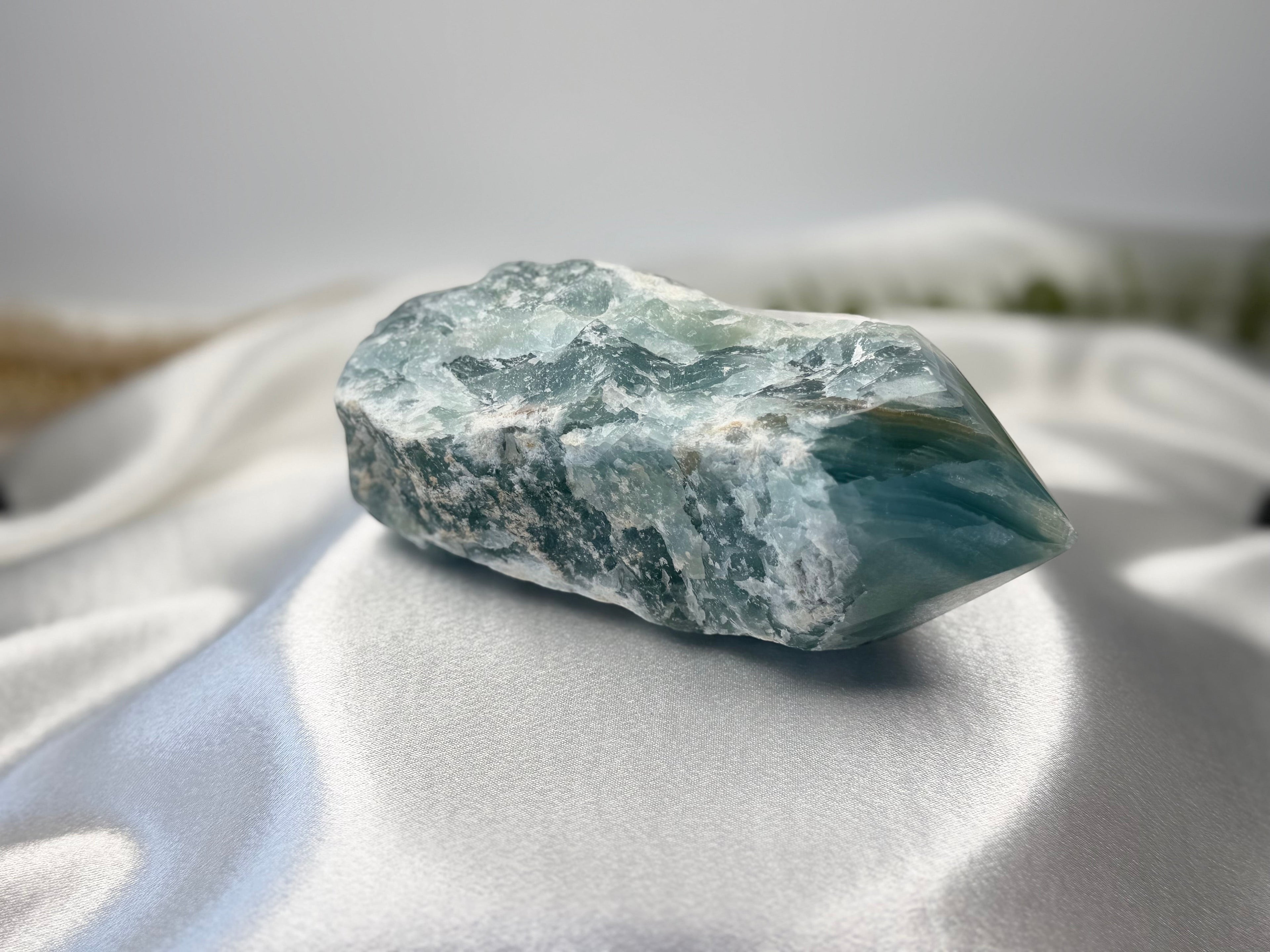 Treasured Energies blue onyx crystal with a raw, natural base and a smooth, polished tower point on white satin.