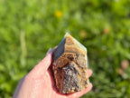 Treasured Energies Blue Onyx tower with a raw, unpolished base and smooth faceted point held in a hand outdoors.