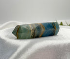 Treasured Energies polished blue onyx crystal tower with natural brown banding resting on white satin fabric.