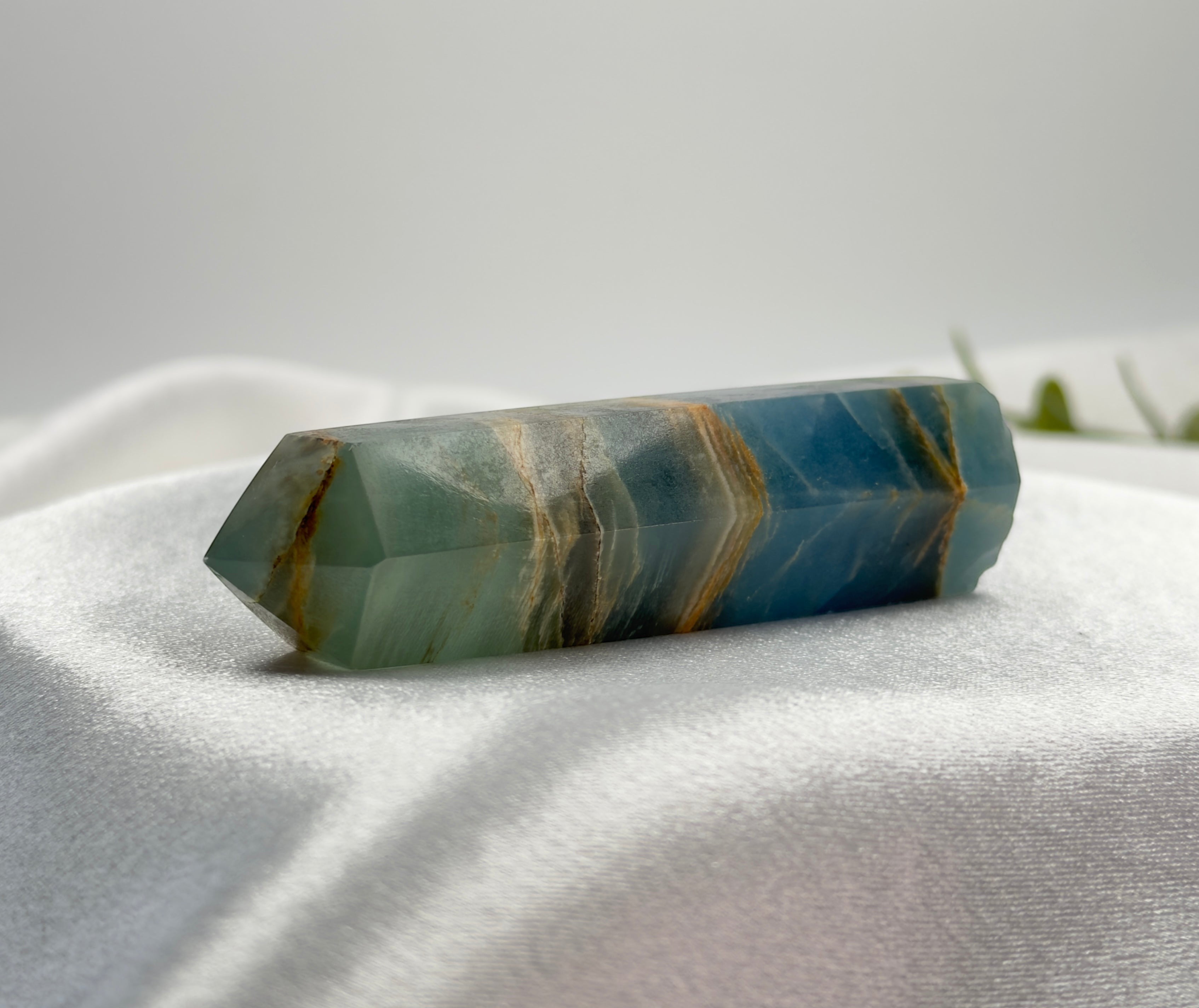 Treasured Energies polished blue onyx crystal tower with natural brown banding resting on white satin fabric.