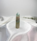 Treasured Energies blue onyx crystal tower with banded patterns and a polished point on a white satin background.