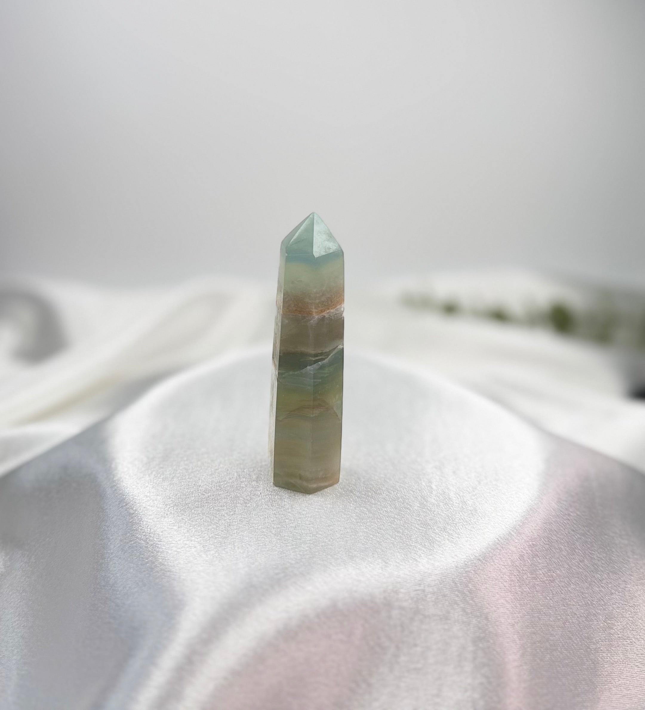 Treasured Energies blue onyx crystal tower with banded patterns and a polished point on a white satin background.