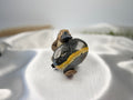 Treasured Energies polished Bumblebee Jasper palm stone with yellow and black bands held by a small platypus figurine.