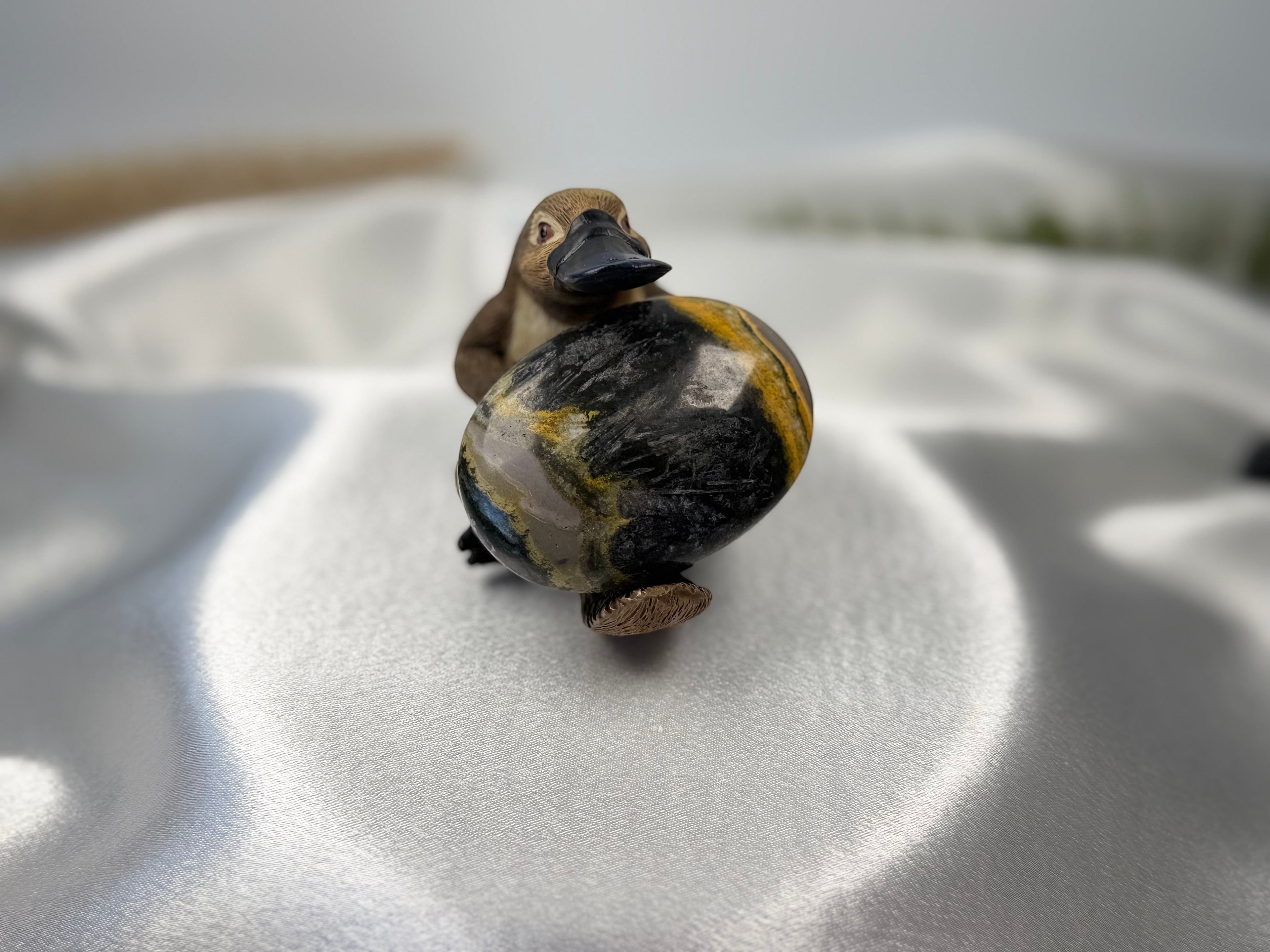 Treasured Energies polished Bumblebee Jasper palm stone held by a small carved wooden platypus figure on white silk.