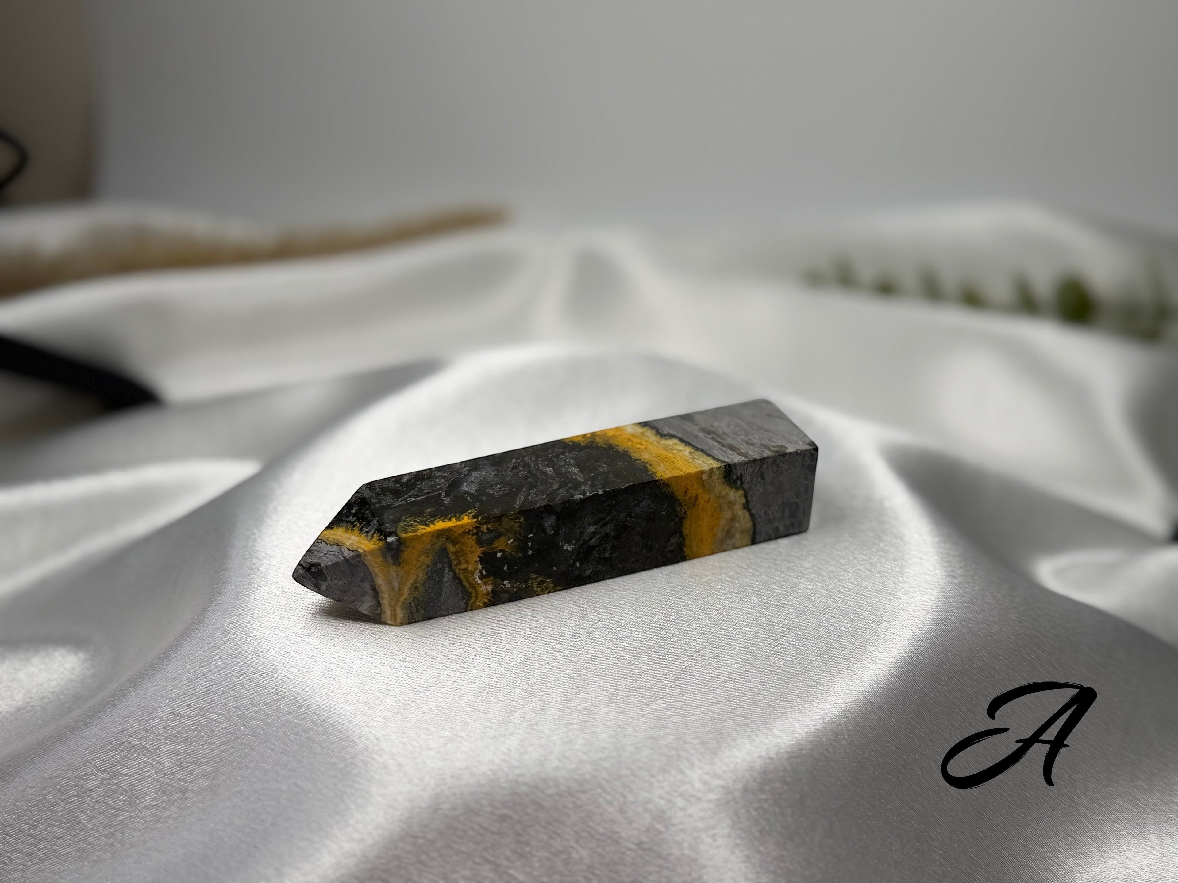 Treasured Energies Bumblebee Jasper crystal tower with vibrant yellow and black volcanic layers on white satin fabric