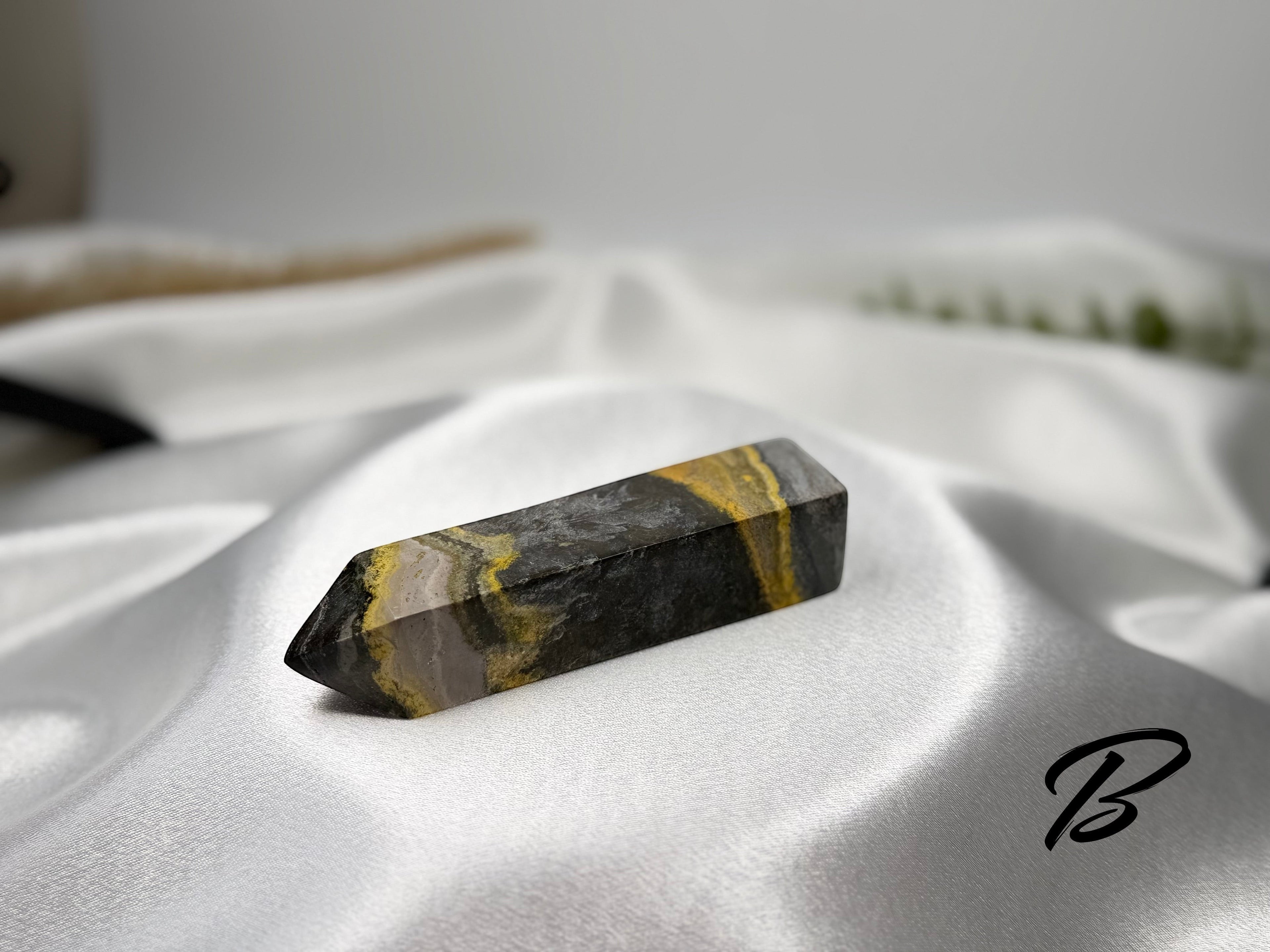 Treasured Energies Bumblebee Jasper crystal tower with vibrant yellow, grey, and black banded patterns on satin fabric.