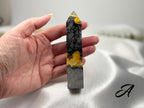 Treasured Energies Bumblebee Jasper crystal tower held in hand, featuring vibrant yellow, black, and grey mineral layers.
