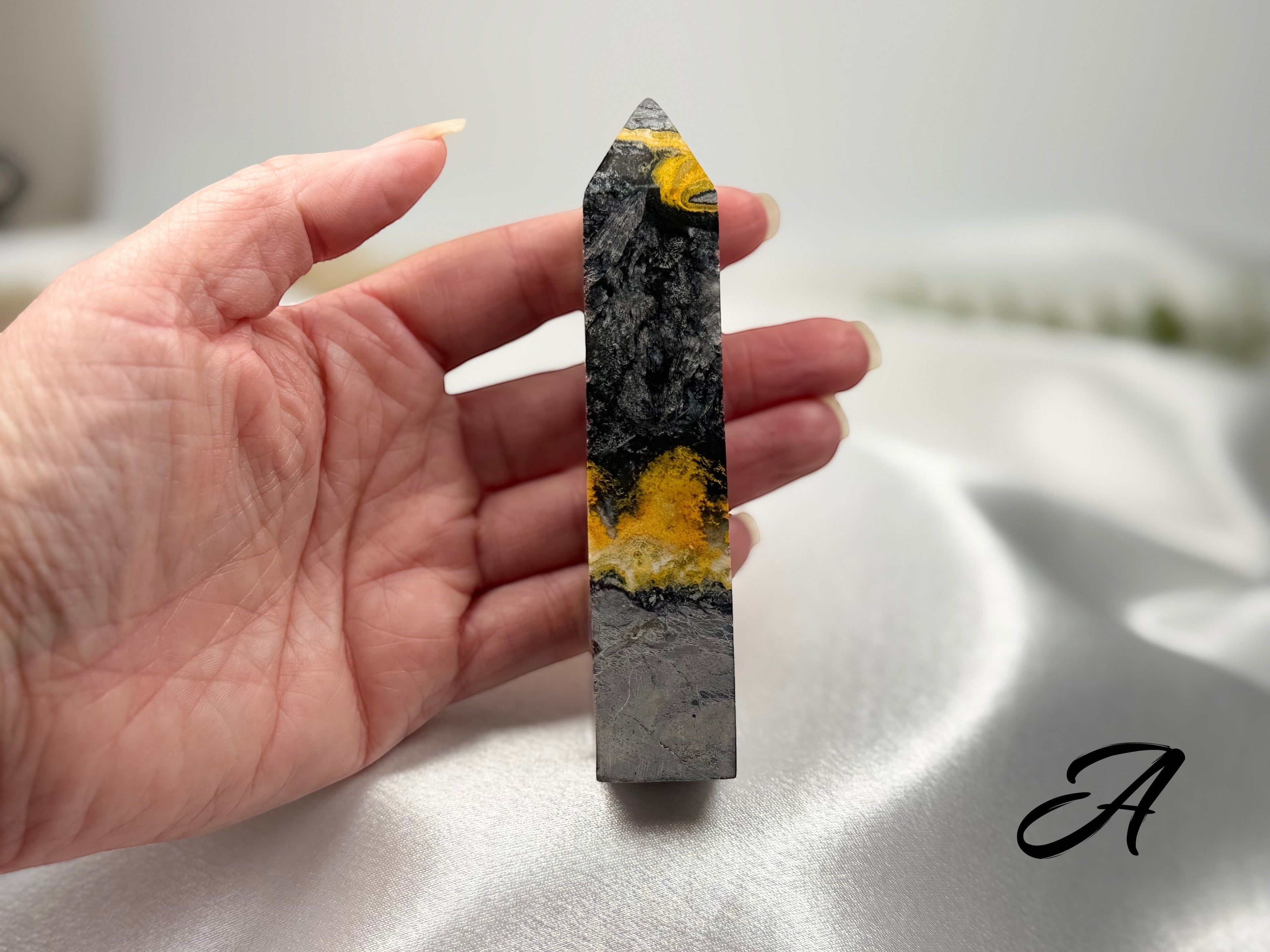 Treasured Energies Bumblebee Jasper crystal tower held in hand, featuring vibrant yellow, black, and grey mineral layers.