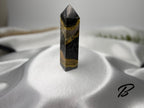 Treasured Energies Bumblebee Jasper crystal tower with black, yellow, and grey banded patterns on a silk background.