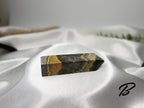 Treasured Energies Bumblebee Jasper crystal tower with yellow, orange, and grey banded patterns on white silk fabric.