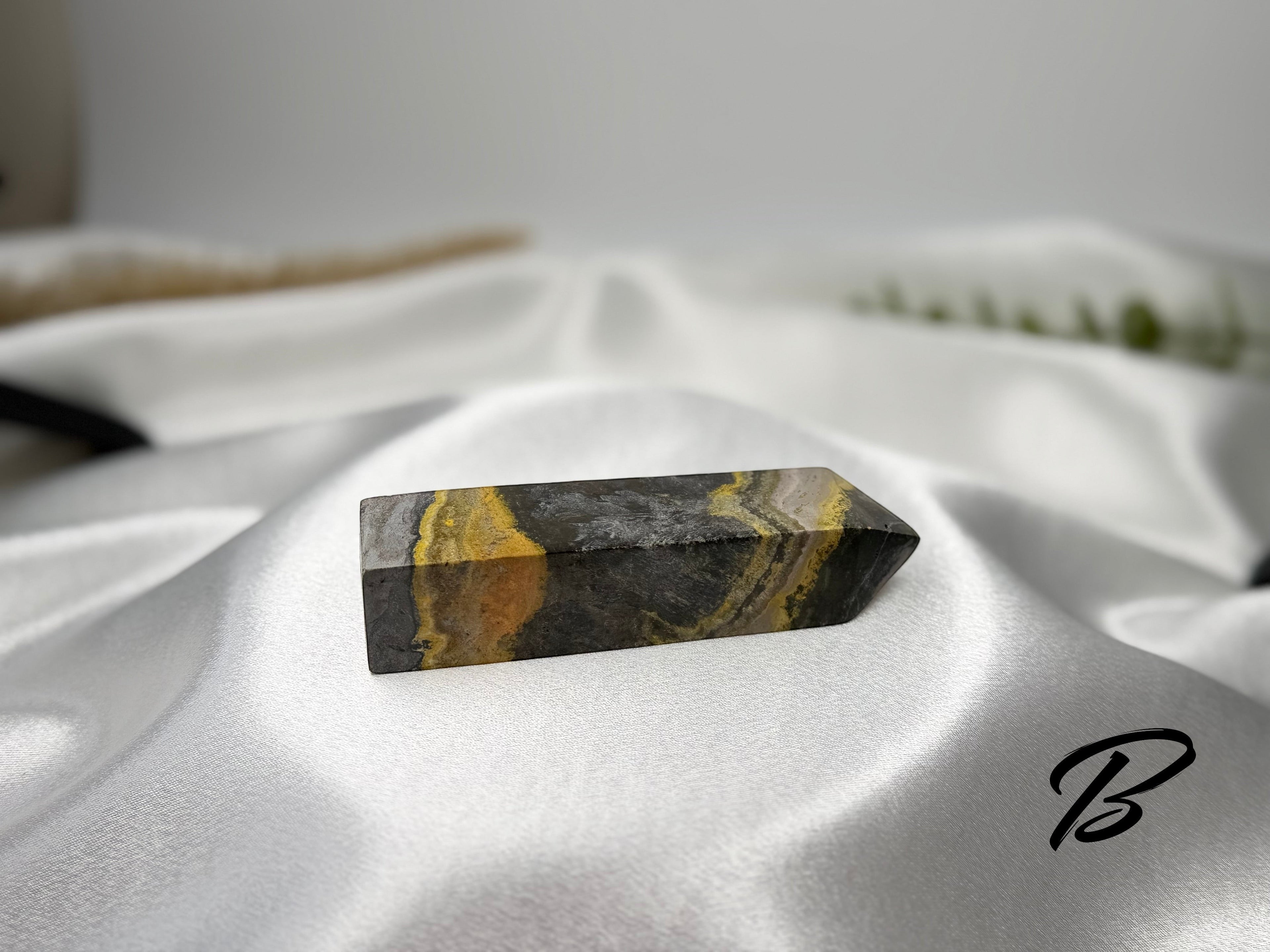 Treasured Energies Bumblebee Jasper crystal tower with yellow, orange, and grey banded patterns on white silk fabric.