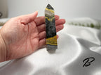 Treasured Energies Bumblebee Jasper crystal tower held in a hand, showing vibrant yellow, grey, and black layers.