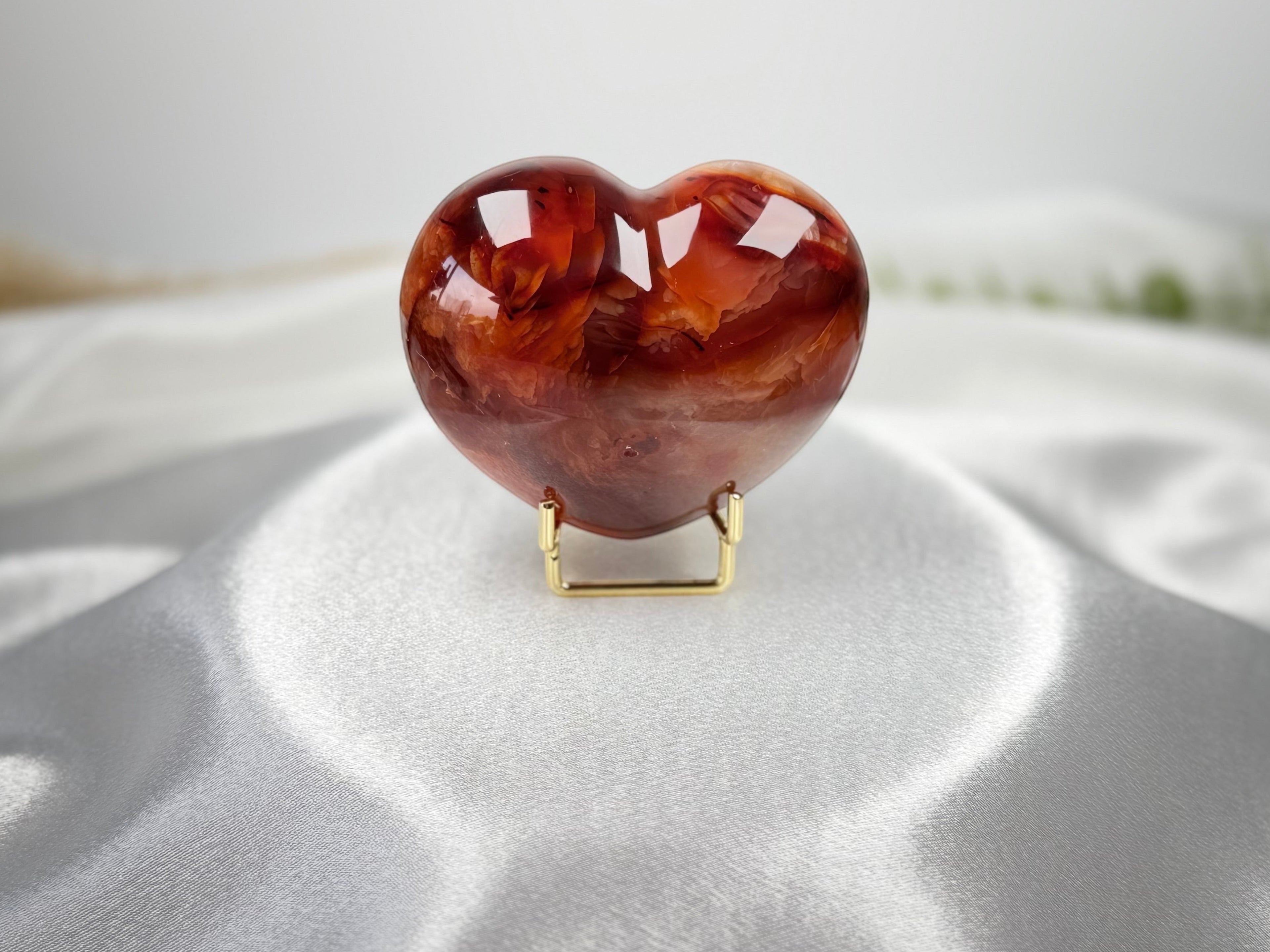 Treasured Energies polished carnelian crystal heart display piece with deep orange and red hues on a gold stand.