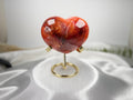 Treasured Energies large polished carnelian crystal heart on a gold metal display stand against a white satin cloth.