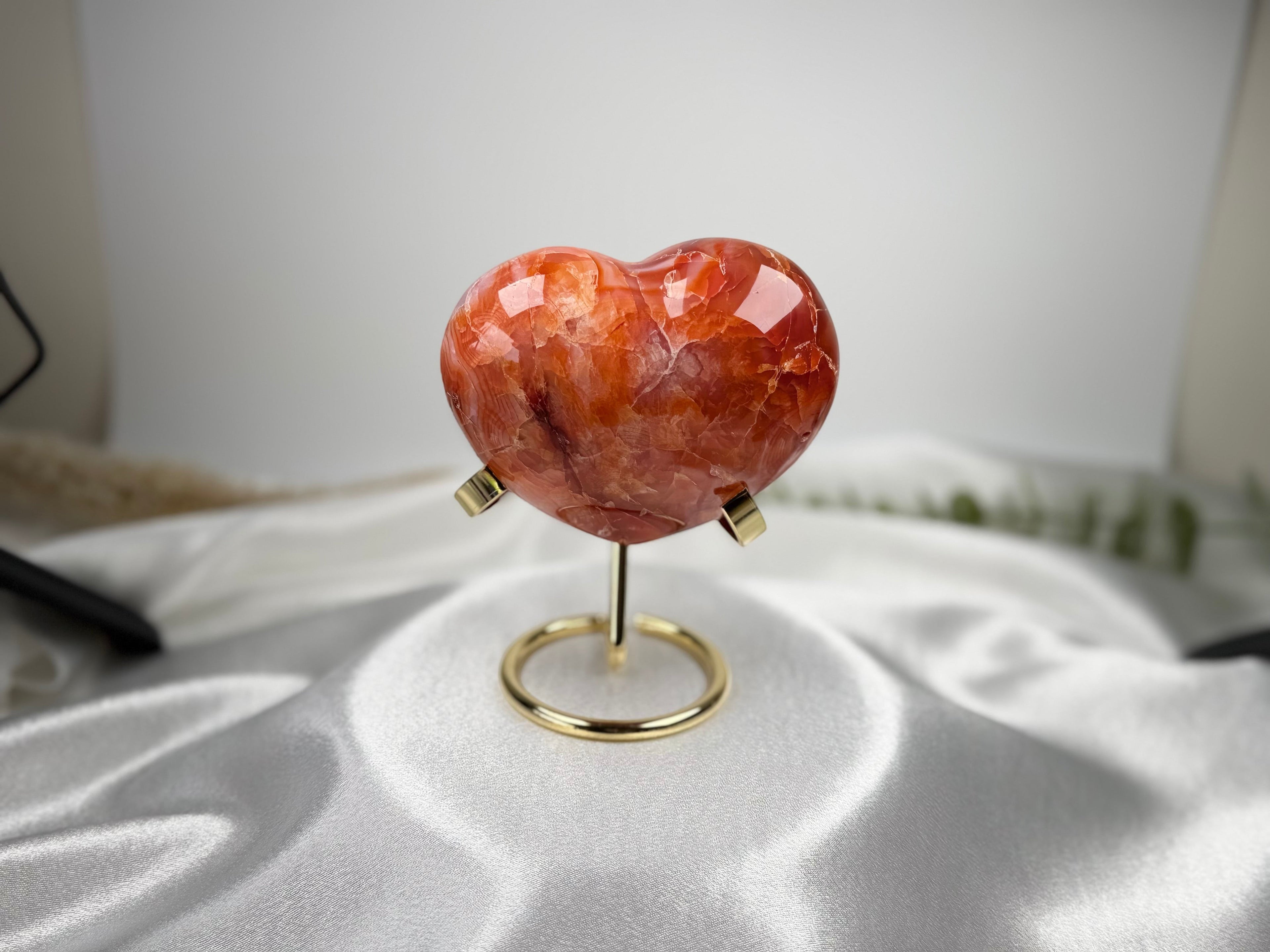 Treasured Energies large polished carnelian crystal heart on a gold metal display stand against a white satin background.