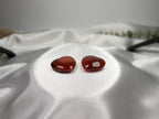 Two polished heart-shaped Carnelian crystals from Treasured Energies displayed on a white satin fabric background.