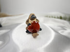 Treasured Energies polished carnelian heart held by a small platypus figurine on a white satin background.