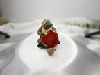 Treasured Energies carnelian heart held by a small carved platypus figurine on a white satin background.