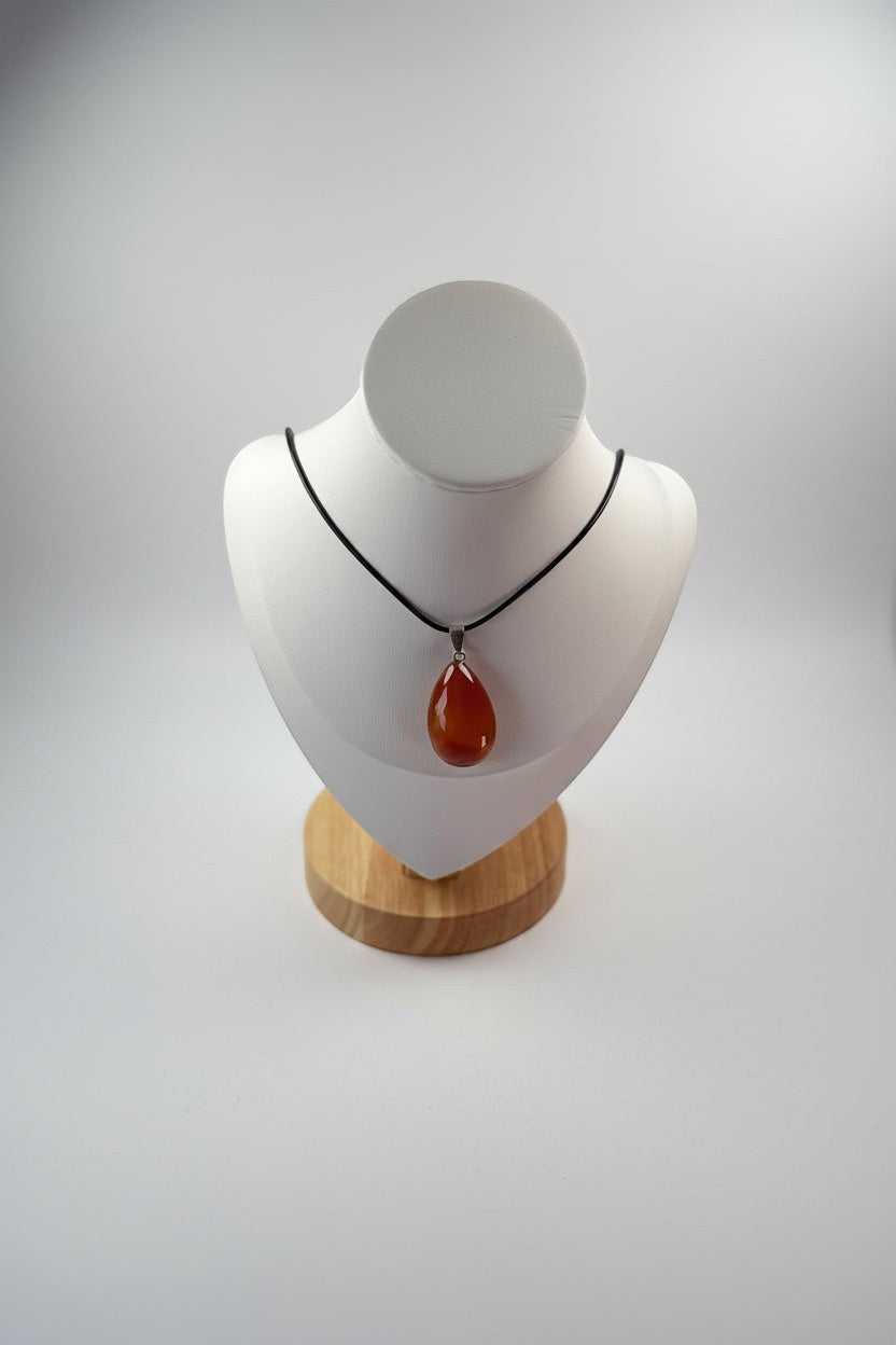 Treasured Energies carnelian teardrop gemstone pendant on a black cord necklace displayed on a white bust